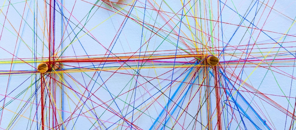 Coloured threads wound around spokes to form a network. Photo by Omar Flores on Unsplash