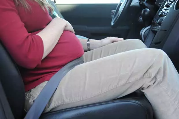 Pregnant woman putting on the seatbelt.