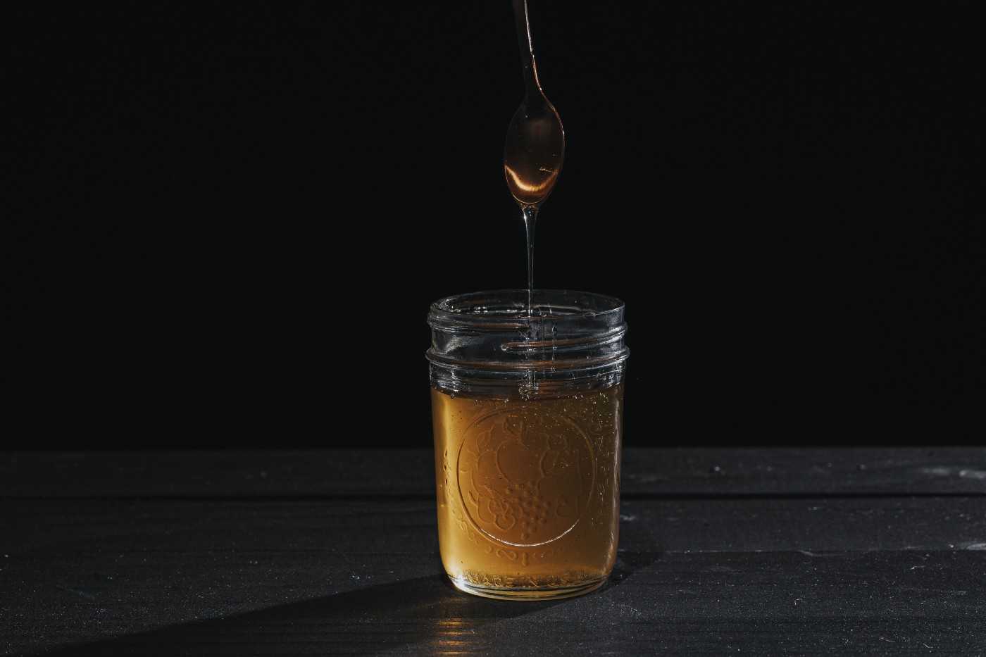 Honey dripping from a spoon into a mason jar