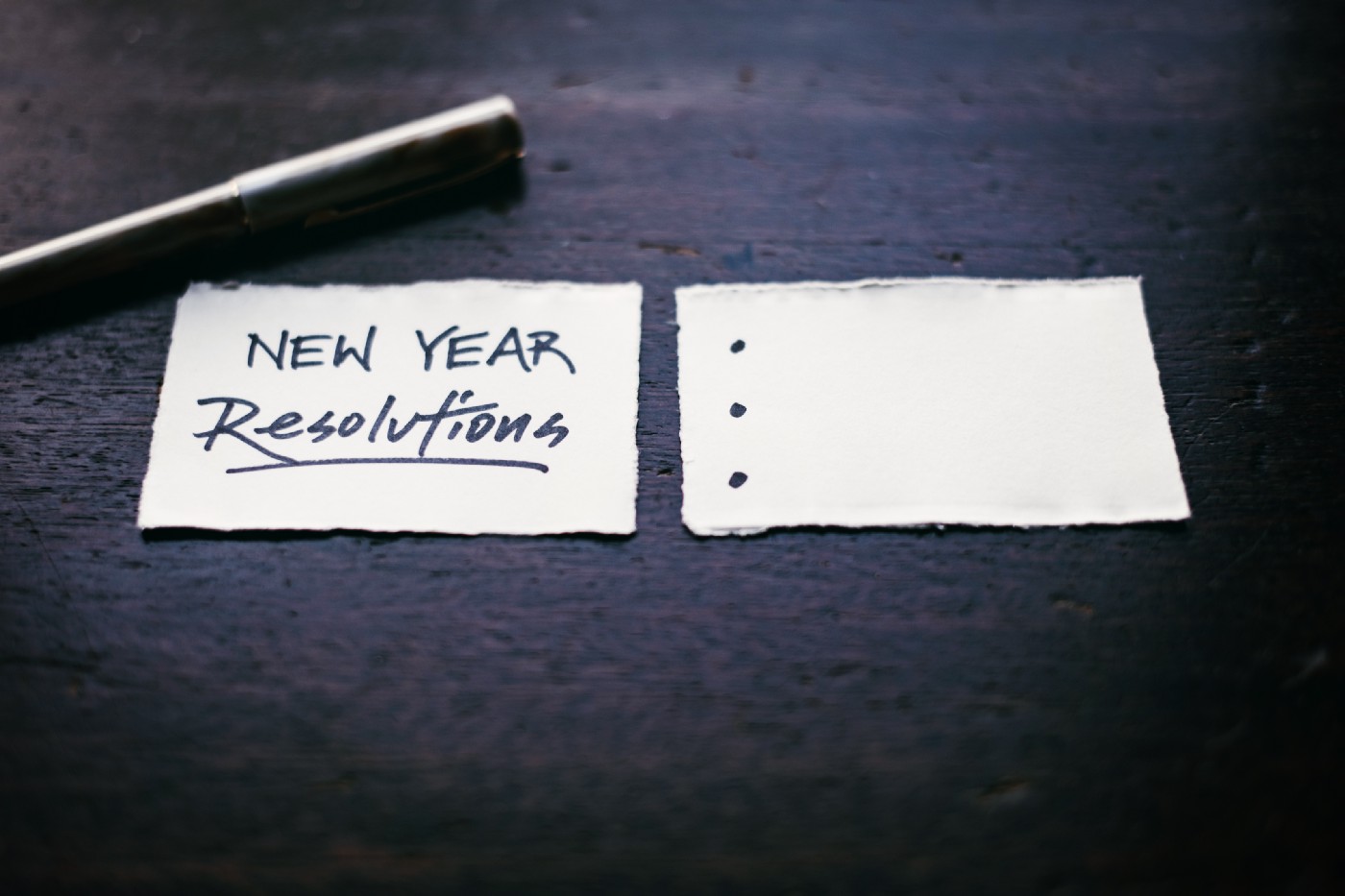 Two pieces of paper next to each other, the first reads ,“New Year Resolutions”. The other is an empty bulleted list.