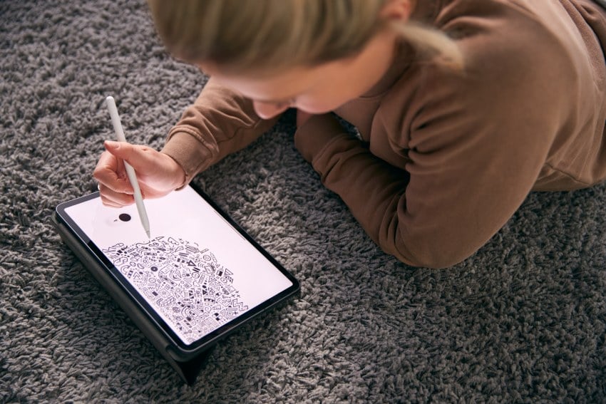 Close Up Of Woman Drawing On Digital Tablet Using Stylus Pen Lying On Carpet At Home