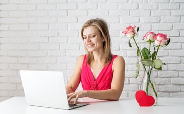woman on a laptop next to valentine’s day roses