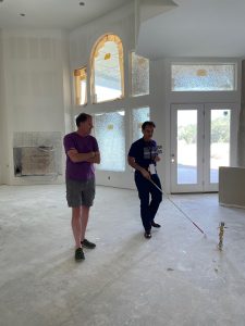 Patrick and Scott in the living room of Patrick's new home during construction. Floors are concrete, dry wall is up, but not painted. Patrick is wearing his axe-con 2023 shirt and is looking sharp in his jeans and boots.