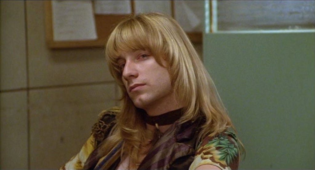 A still from the movie Hair, showing a blonde man with long hair looking sassy
