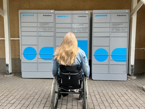 Wheelchair user sitting in front of post boxes, back turned towards the camera.