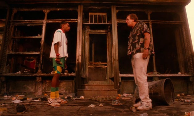 two men, one Black (left) and one white (right) face off in front of a burnt out diner