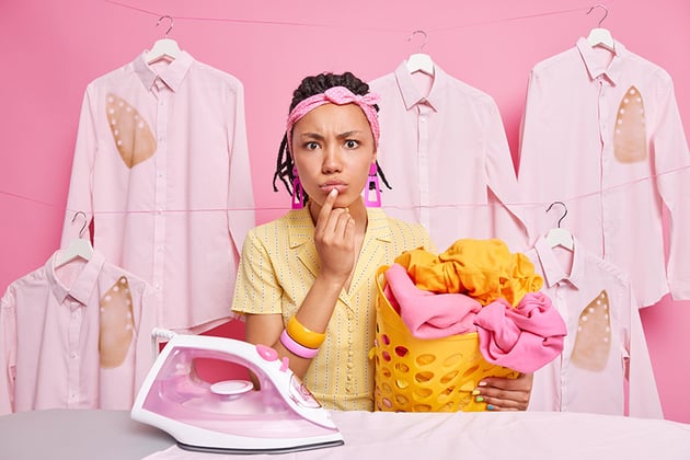 Serious attentive dark skinned young woman holds basket full of washed laundry irons linen looks dir by