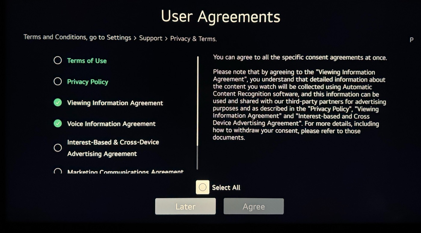 The LG TV's User Agreements screen: 6 different user agreements are available to be agreed to, each with a radio button. The Terms of Use and Privacy Policy items are shown in green text, but the rest are white text. Viewing Information Agreement and Voice Information Agreement are pre-selected, implying they can't be changed. 